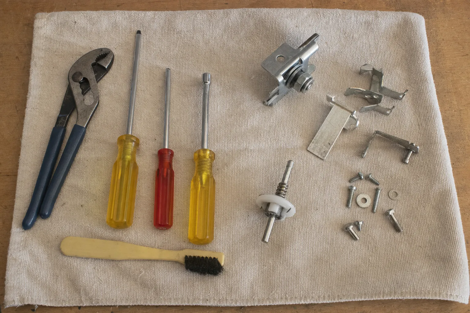 Groove-joint pliers, three screwdrivers, a small brush, a spring-loaded stem with a white collar, brackets, clips and screws on canvas